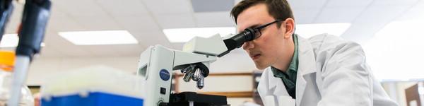 Male student in a lab coat looking through a microscope.