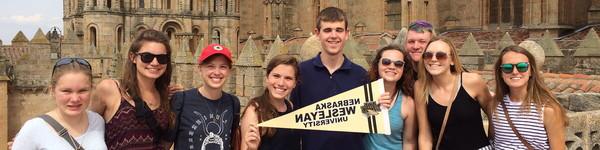 A blind man holds a Nebraska Wesleyan pennant with other students in front of a castle.